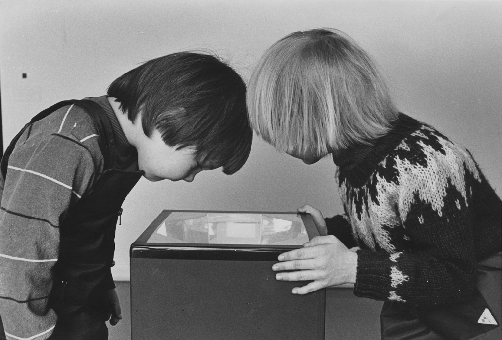 Kaksi lasta vanhassa valokuvassa kurkistamassa rasiaan ylhäältä päin.